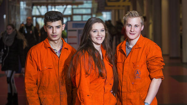 Drie Aventus-studenten staan in hun oranje overall in de Hi street